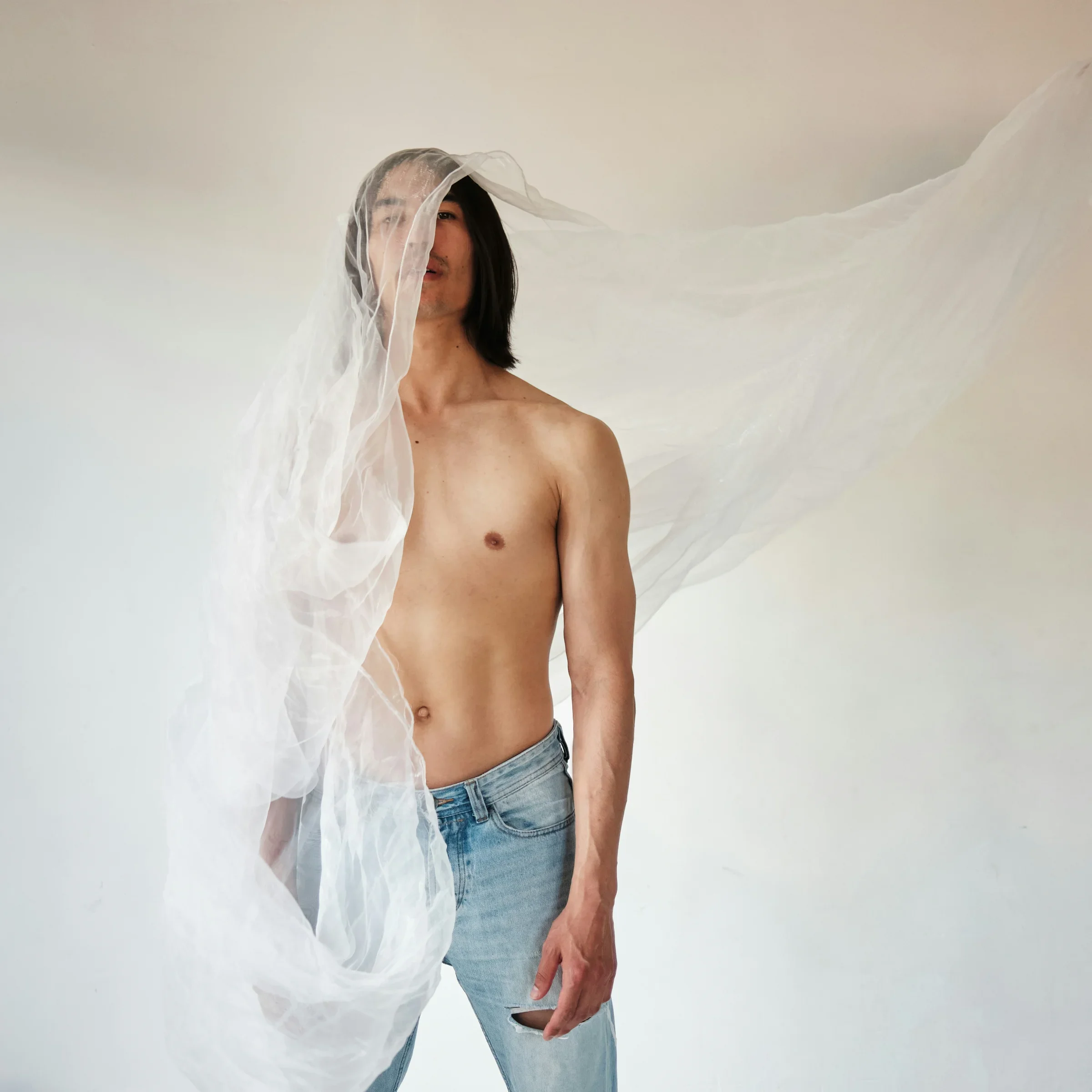 A man gazing through a sheer translucent veil — a living presence the eye cannot read, its state hidden behind a membrane it wears itself.